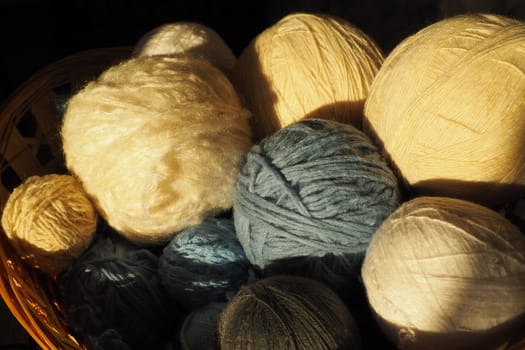 White, beige and blue woolen and acrylic threads wound into a ball or skein. Several skeins of light yarn in a basket. Knitting as a hobby. A clew of thread