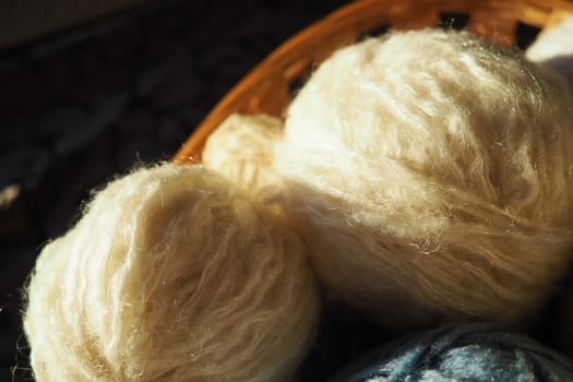 White, beige and blue woolen and acrylic threads wound into a ball or skein. Several skeins of light yarn in a basket. Knitting as a hobby. A clew of thread