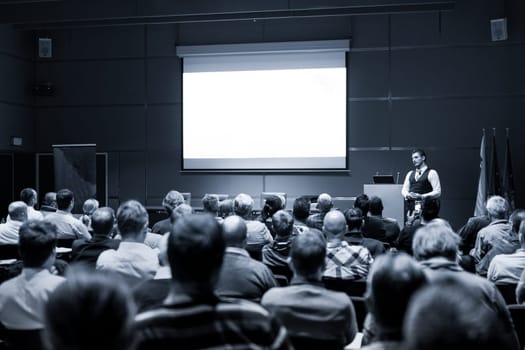 Speaker Giving a Talk at Business Meeting. Audience in the conference hall. Business and Entrepreneurship concept. Black and white blue toned image.