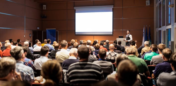 Speaker giving a talk in conference hall at business meeting event. Rear view of unrecognizable people in audience at the conference hall. Business and entrepreneurship concept.