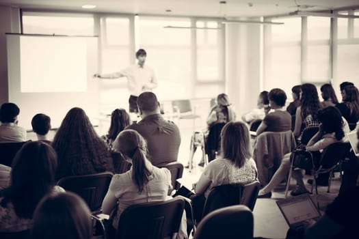 Business and entrepreneurship symposium. Speaker giving a talk at business meeting. Audience in conference hall. Rear view of unrecognized participant in audience.