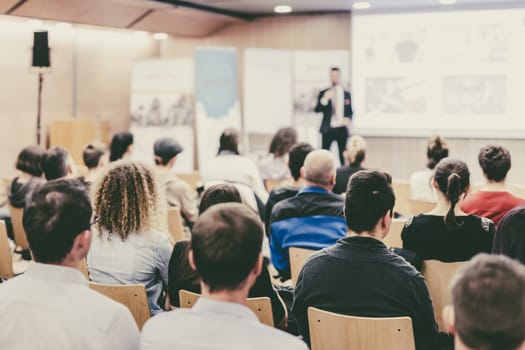 Speaker giving a talk in conference hall at business event. Audience at the conference hall. Business and Entrepreneurship concept. Focus on unrecognizable people in audience.