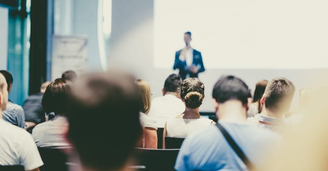 Male speaker giving a talk in conference hall at business event. Audience at the conference hall. Business and Entrepreneurship concept. Focus on unrecognizable people in audience.