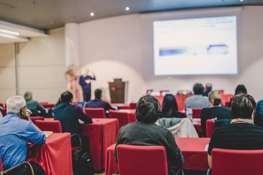 Speaker Giving a Talk at Business Meeting. Audience in the conference hall. Business and Entrepreneurship. Focus on unrecognizable people from rear.