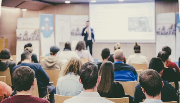 Speaker giving a talk in conference hall at business event. Audience at the conference hall. Business and Entrepreneurship concept. Focus on unrecognizable people in audience.