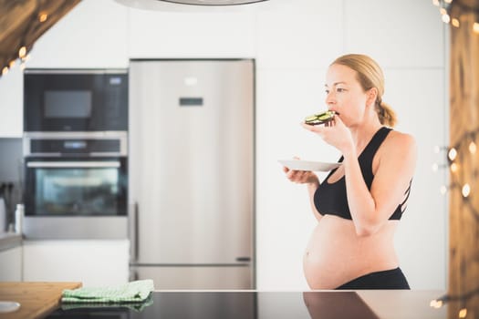 Beautiful sporty fit young pregnant woman having a healthy snack in home kitchen. Healty lifestyle concept