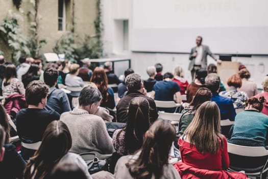 Male speaker giving presentation in lecture hall at university workshop. Audience in conference hall. Rear view of unrecognized participant. Scientific conference event. Copy space on whitescreen.
