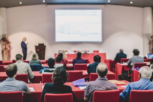 Speaker Giving a Talk at Business Meeting. Audience in the conference hall. Business and Entrepreneurship. Focus on unrecognizable people from rear.