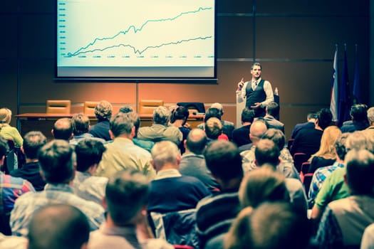 Speaker giving a talk in conference hall at business meeting event. Rear view of unrecognizable people in audience at the conference hall. Business and entrepreneurship concept.