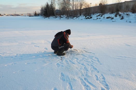 Fisherman on winter fishing. A man sits near a hole in a frozen lake waiting for a bite. Snow on ice. Bottom fishing for perch. Frosty January evening