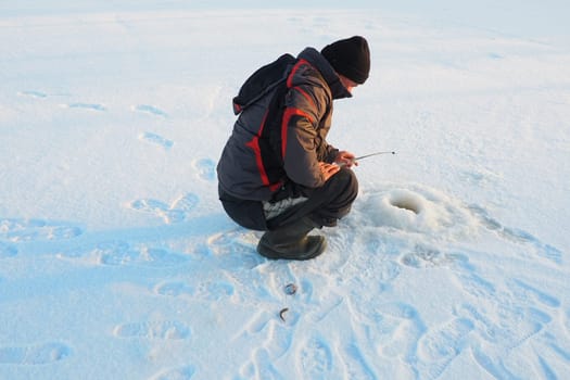 Fisherman on winter fishing. A man sits near a hole in a frozen lake waiting for a bite. Snow on ice. Bottom fishing for perch. Frosty January evening