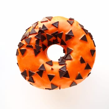 Halloween donut with orange frosting and chocolate triangles as a sweet decorative topping. Childrens holiday sweets on a white background. Trick or treat. All Hallows Eve. All Saints Eve Doughnut.