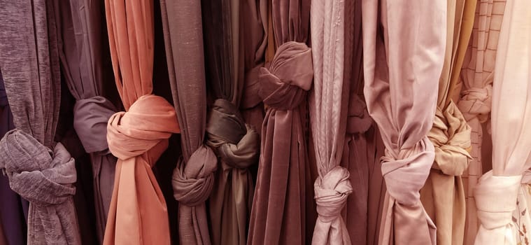 Curtain and fabric for drapery and interior decoration. Samples of fabrics in the store are hung vertically and tied in knots. Curtains in the showcase. Curtains in pink, beige, brown warm tones