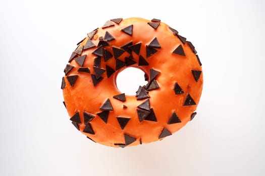 Halloween donut with orange frosting and chocolate triangles as a sweet decorative topping. Childrens holiday sweets on a white background. Trick or treat. All Hallows Eve. All Saints Eve Doughnut.