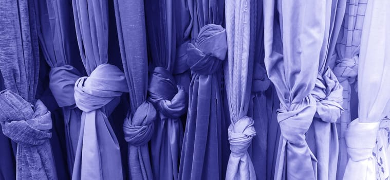 Curtain and fabric for drapery and interior decoration. Samples of fabrics in the store are hung vertically and tied in knots. Curtains in the showcase. Curtains of blue, purple cold tones