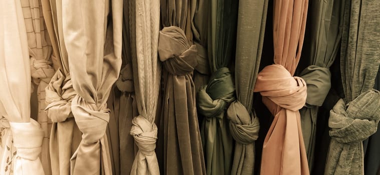 Curtain and fabric for drapery and interior decoration. Samples of fabrics in the store are hung vertically and tied in knots. Curtains in the showcase. Beige, brown, gray, yellow and peach fabric