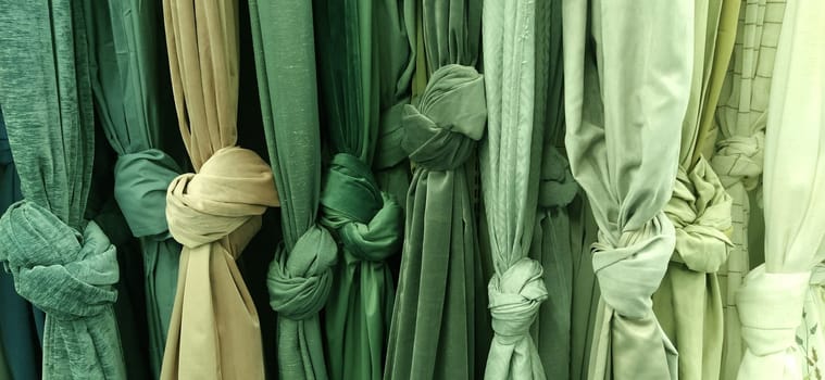 Curtain and fabric for drapery and interior decoration. Samples of fabrics in the store are hung vertically and tied in knots. Green, beige colored and white curtains in the showcase. Store shelves