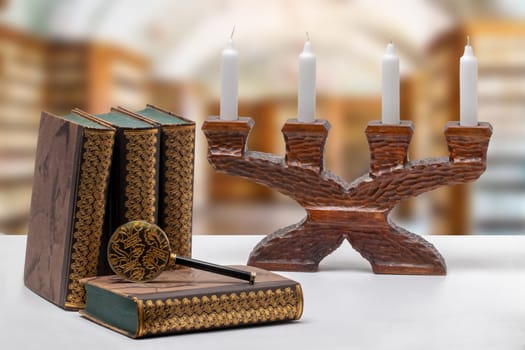 Ancient books with a magnifying glass and a antique wooden candle holder on a bright table isolated over abstract blurred library. University, history, memory and knowledge concept.