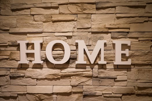On a wall covered with narrow stones, the word "Home"" is written."