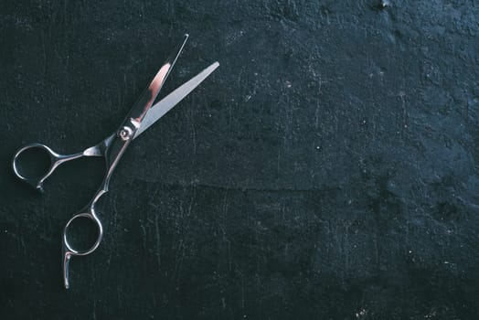 Hairdresser scissors on dark rustic background with copyspace from above. Professional hairstyle salon studio background design. Top view of haircut tool on black.