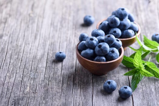 Bowl of fresh blueberries on rustic wooden table. Healthy organic seasonal fruit background. Organic food blueberries and mint leaf for healthy lifestyle.