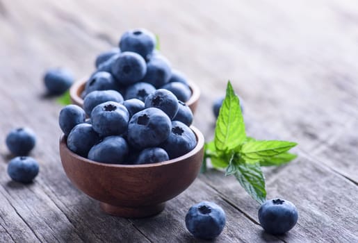 Bowl of fresh blueberries on rustic wooden table. Healthy organic seasonal fruit background. Organic food blueberries and mint leaf for healthy lifestyle.