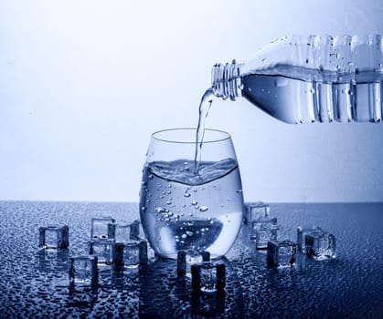 Pouring fresh drinking mineral water from plastic bottle. Glass filled with water over white background.
