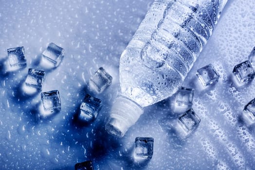 Fresh drinking mineral water in plastic bottle with ice cubes and iced drops. Healthy living concept from above.