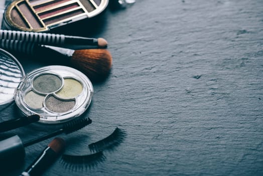 Professional makeup artist set on black background with copyspace. Top view of cosmetics product kit with eye shadow palette, mascara, brushes, lipstick, face powder and eye lushes.