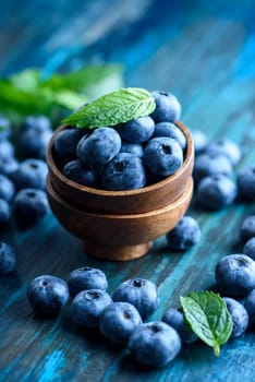Bowl of fresh blueberries on rustic wooden table. Healthy organic seasonal fruit background. Organic food blueberries and mint leaf for healthy lifestyle.