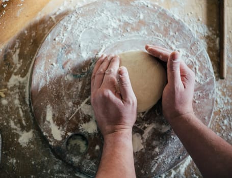 Top view of man kneading pizza dough in the kitchen. Closeup on baker's hands preparing loaf of bread.