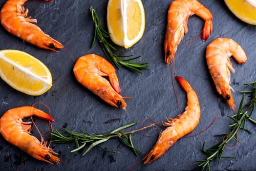 Top view of shrimps with lemon and rosemary on black background. Seafood dine cooking background.