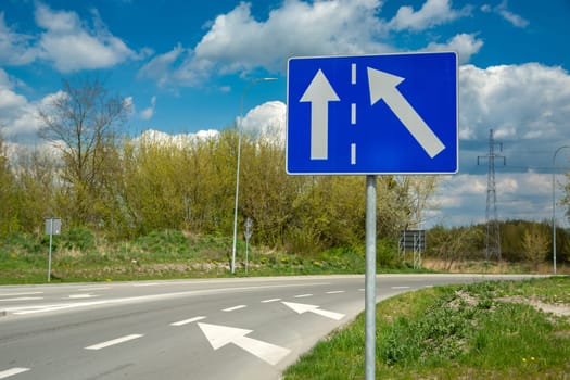 Blue rectangle road sign and white arrows, spring day