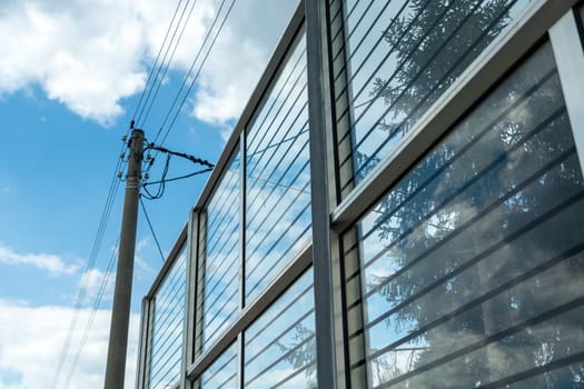 Electric pole standing by glass noise barriers and sky.