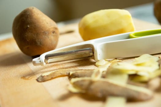 Peeler and potatoes with peelings on the wooden table