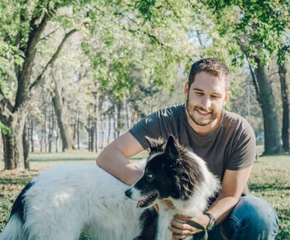 Man with his dog playing outdoor in the park. Young owner hugs his pet in nature.