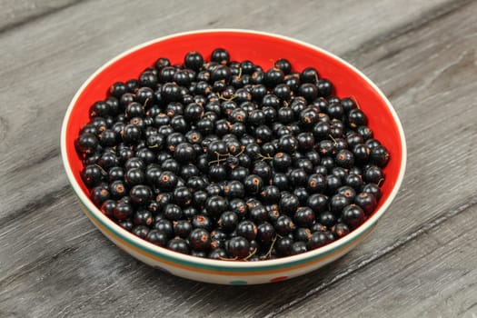 Bowl with red inside, full of blackcurrant, on wooden desk.