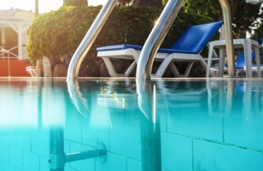 Partially underwater photo, steel handrails at entry to swimming pool, backlight sun shining in background. Vacation / relax image.
