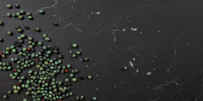 Tabletop view, Black pepper (Piper nigrum) spice spilled on dark marble like board. Turkish green / blue peppercorn variant. Banner with space for text on right.