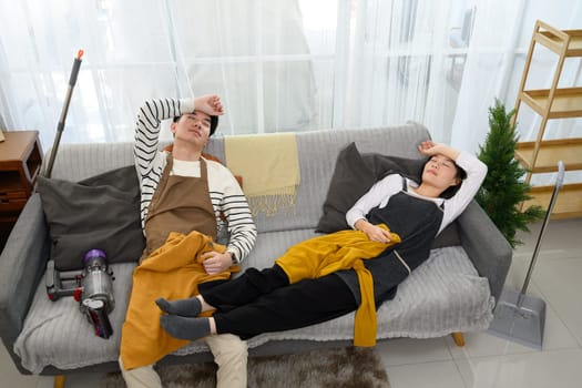 Tired couple lays back on the couch, overwhelmed after tidying up their home.