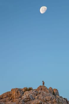 Wild goat on the rocks of La Sierra Del Torcal de Antequera National Park, Malaga, Spain. Morning moon over blue sky