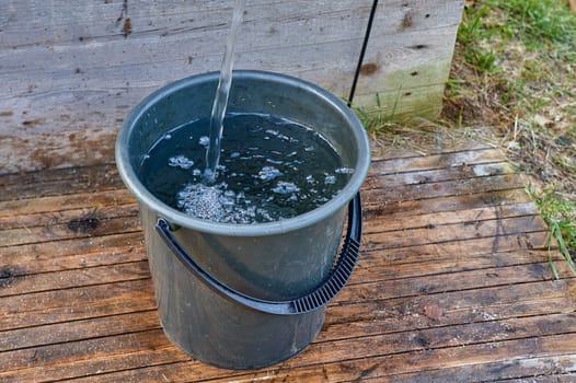 a black plastic bucket is filled with water from the pump. High quality photo
