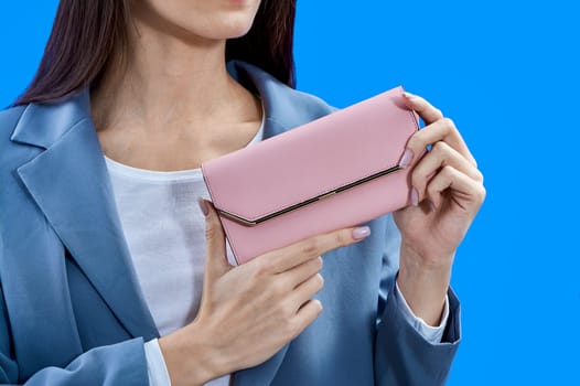 A beautiful young woman is holding a pink purse on a blue background, copy space. High quality photo