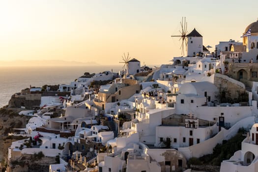 Oia, Santorini, Greece - June 28, 2021: Whitewashed houses and windmills in Oia in warm rays of sunset on Santorini island. Greece