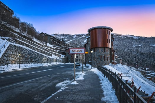 Soldeu sign at entrance to the town, pine forest and snow capped mountain range in background. Ski winter holidays in Andorra, Pyrenees Mountains