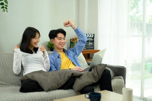 Happy excited young couple celebrating a victory while looking something on laptop.