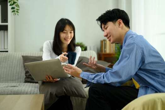 Happy young couple enjoys a conversation and using laptop in their cozy living room.