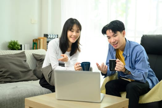 Young couple enjoying coffee and browsing the internet on laptop in their living room.