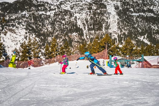 Ski instructor helping out and teaching young kids how to ski, El Tarter green slope. Winter holidays in Andorra, Pyrenees Mountains, Grandvalira