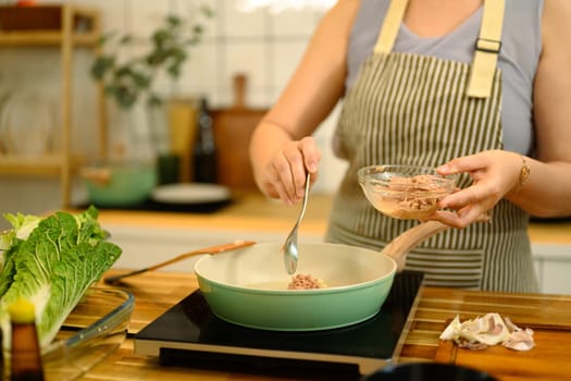 Close up of adult woman adding minced meat into a frying pan while preparing a homemade meal.